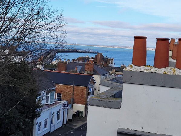 A coastal town with buildings overlooking the sea, a bridge in the distance, and a chimney on a rooftop. - Nelson's View (Ryde)