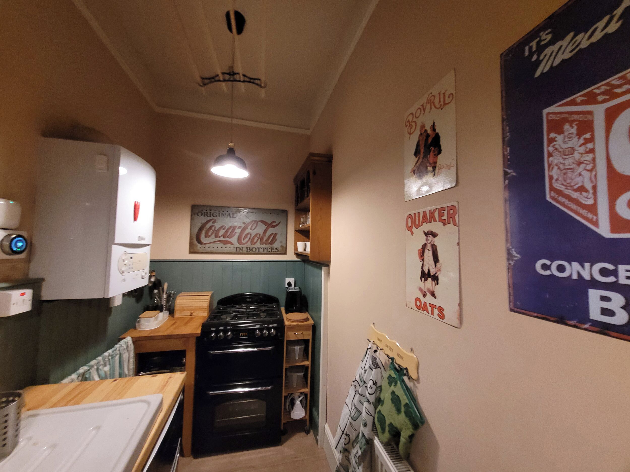 Una cocina compacta con refrigerador, estufa y horno empotrado. Hay carteles antiguos y un letrero de 'Quaker Oats' en la pared.