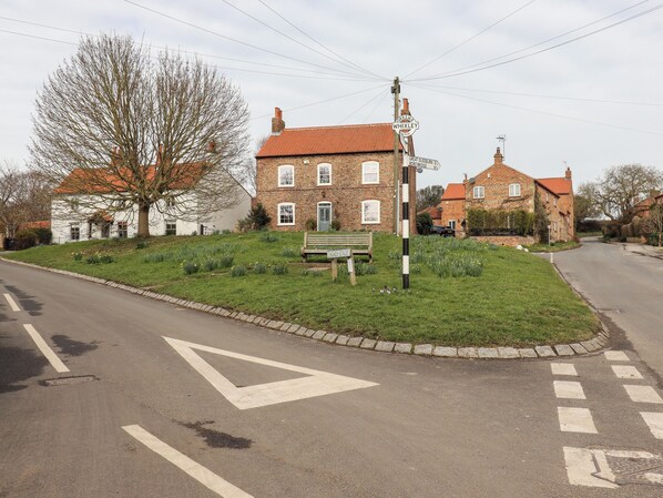 A quiet street with a bench, a signpost, and a grassy area with flowers. - Duckstone Cottage (York)