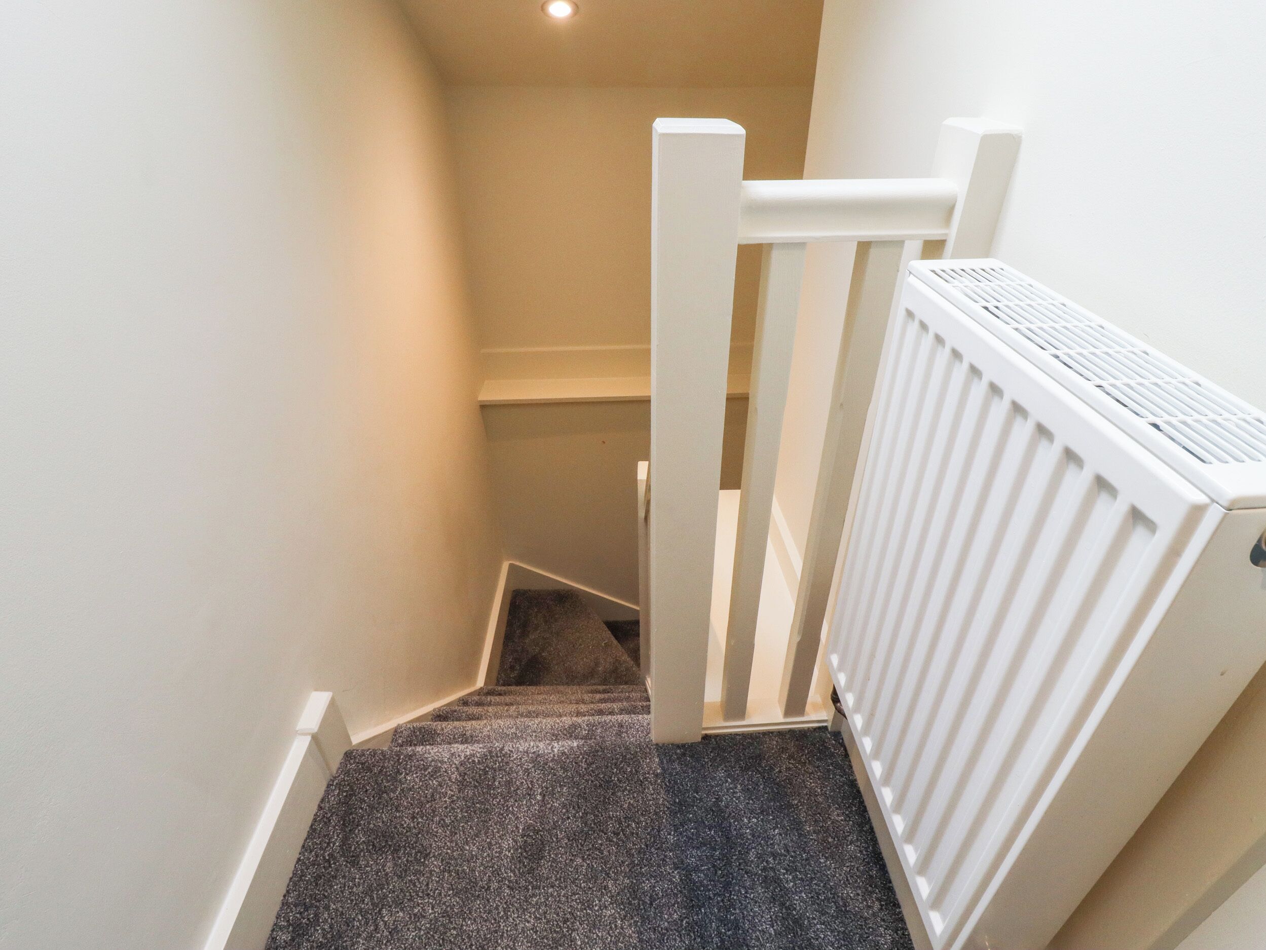 En smal trappe med et møbleringstapetage, hvide gelændere og en hvid radiator til højre.