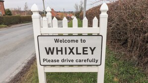 Un panneau d’accueil à l’entrée de WHIXLEY, avec un message invitant les conducteurs à faire preuve de prudence.