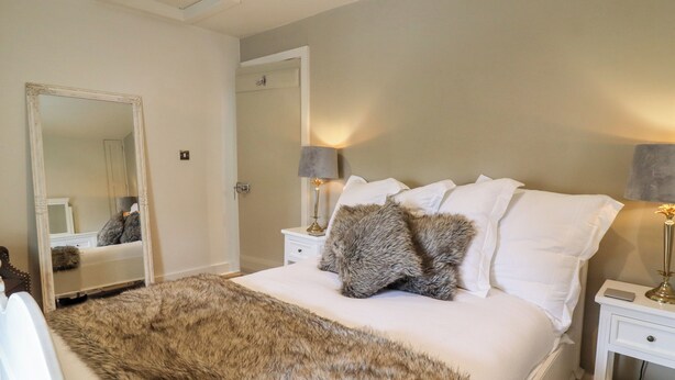 Une chambre à coucher avec un grand lit, deux tables de chevet, un miroir et un plaid en fausse fourrure.