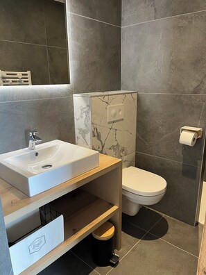 Casa de banho moderna com lavatório branco, salpicão de mármore e sanita.