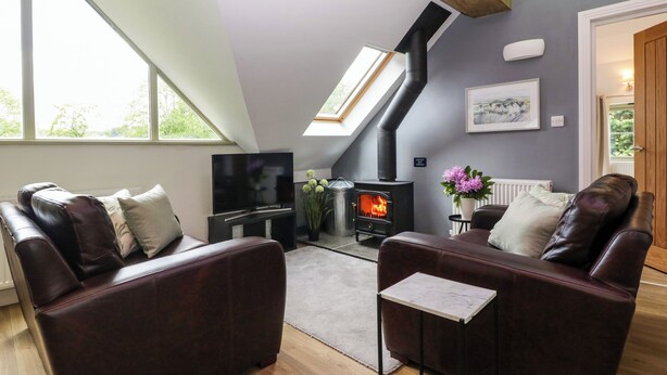 A cozy living room with a fireplace, leather sofas, a TV, and a skylight. - The Coach House (Ludlow)