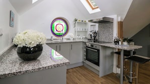 A modern kitchen with a skylight, granite countertops, a built-in oven, and a bar area. - The Coach House (Ludlow)