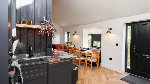 A modern kitchen with dark cabinetry, a marble countertop, and a wooden dining area with a table and chairs. - The Haven (Scarborough)