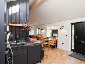 Una cocina moderna con armarios oscuros, encimera de mármol y zona de comedor de madera con una mesa y sillas.