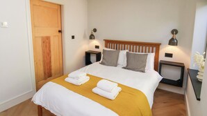 A neatly made bed with white linens and a mustard-colored throw, flanked by two bedside tables with lamps, in a room with wooden beams on the ceiling and a wooden door. - The Haven (Scarborough)