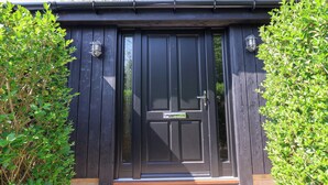 A dark wooden door with a glass panel and a small window, flanked by two wall-mounted light fixtures. - The Haven (Scarborough)