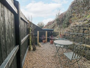 A patio area with a metal table and chairs, surrounded by a wooden fence and potted plants. - The Haven (Scarborough)