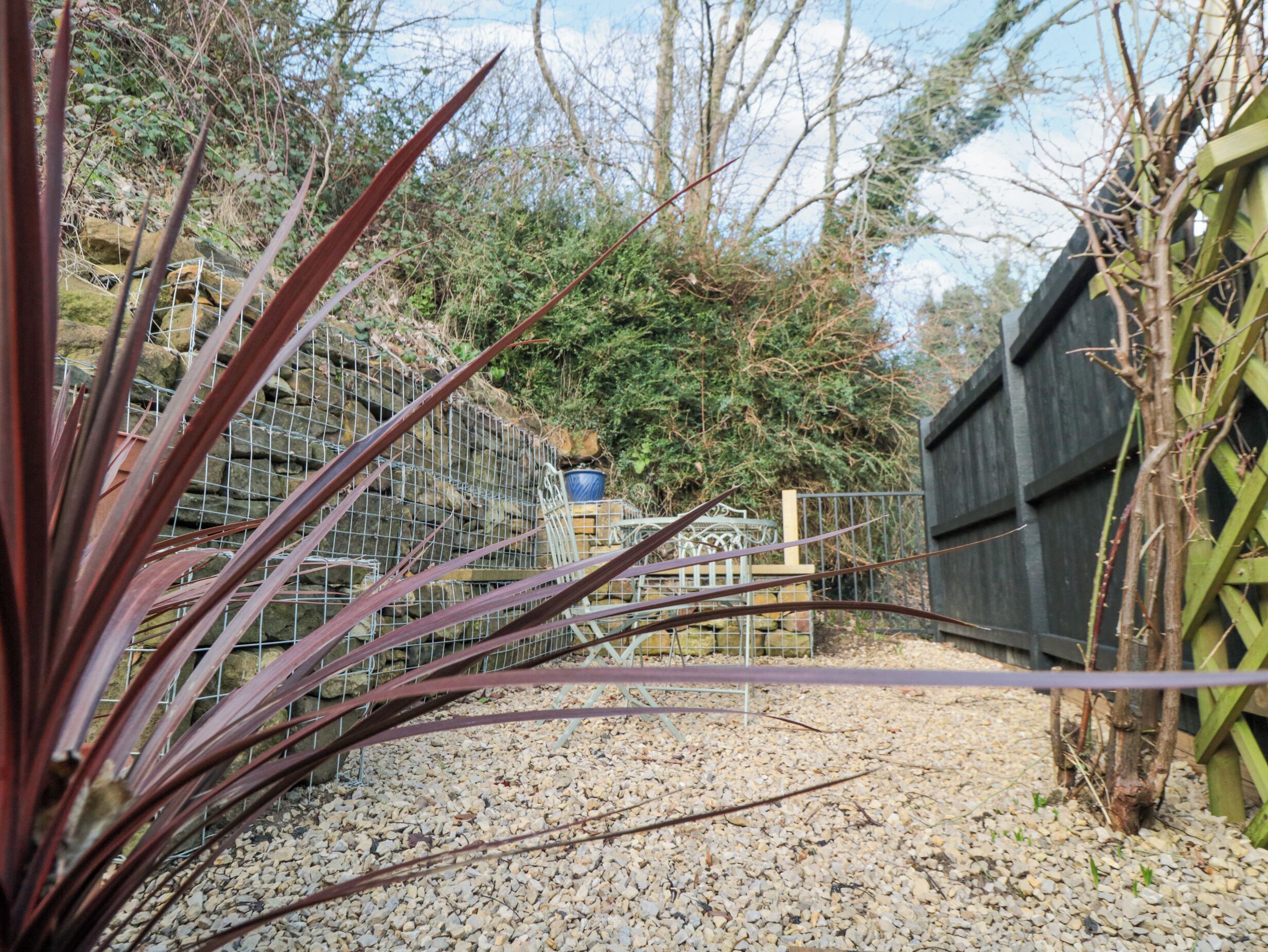 A garden area with a gravel path, a metal fence, and a wooden structure in the background.
