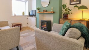A cozy living room with a fireplace, a television, and a green wall with a mirror and artwork. - Bear Cottage (Matlock)