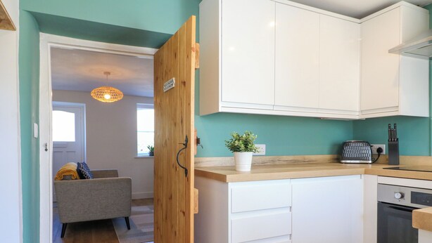 A modern kitchen with white cabinets, a wooden door, a toaster, and a potted plant. - Bear Cottage (Matlock)