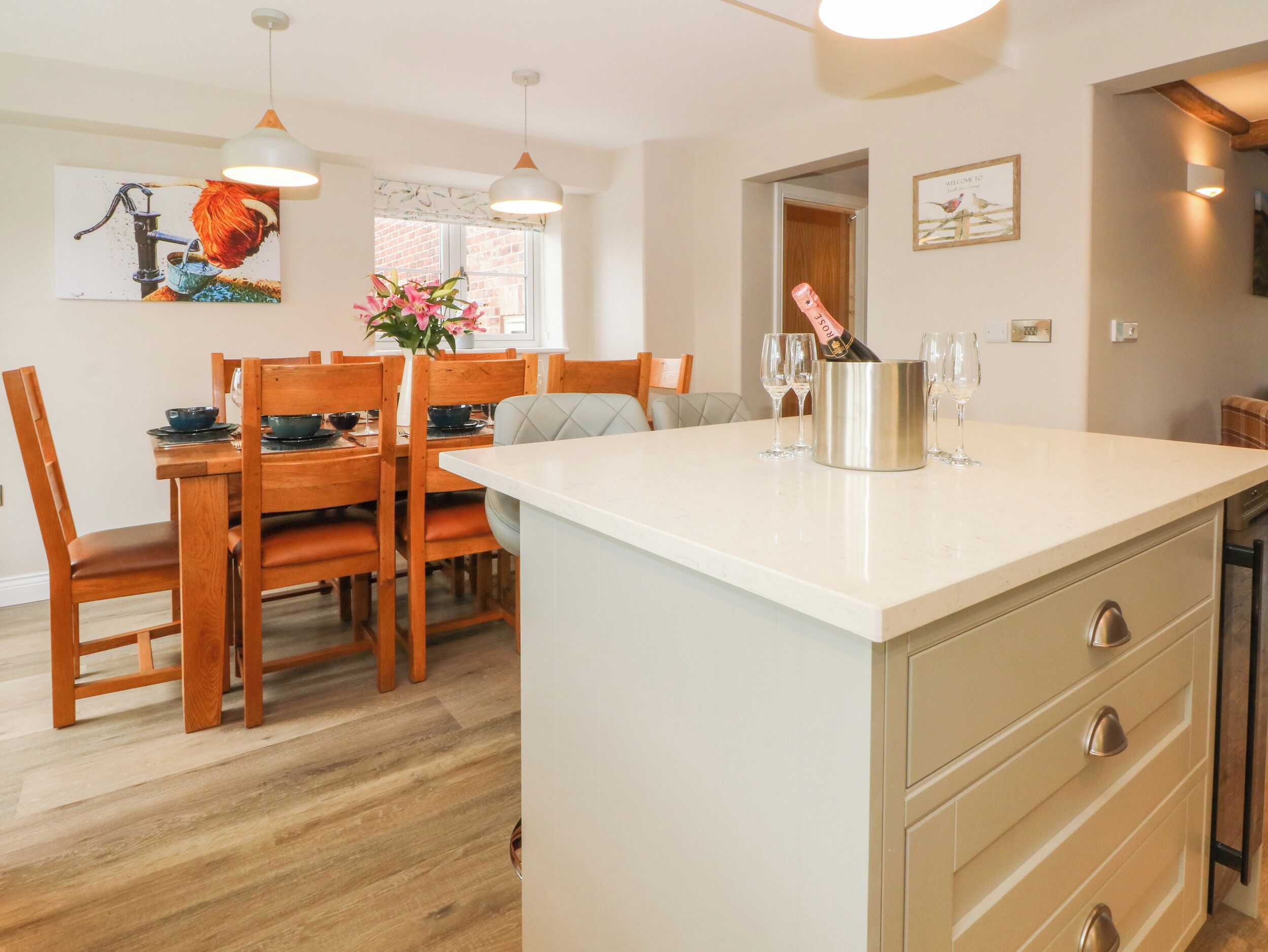 A modern kitchen with wooden furniture, a white countertop, and a dining area with a table and chairs.