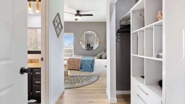 Un couloir menant à une chambre à coucher équipée d’un lit, d’un miroir rond et d’un ventilateur de plafond.