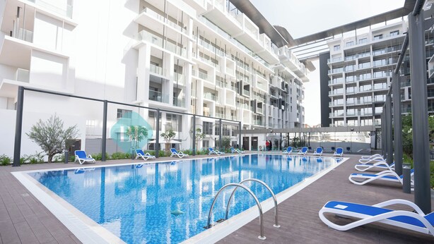 Een modern hotelzwembad met helderblauw water, ligbedden en een meerlaags gebouw met balkons.