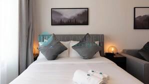 Een netjes opgemaakt bed met witte lakens en twee kussens, een bedlampje en een ingelijst foto aan de muur.