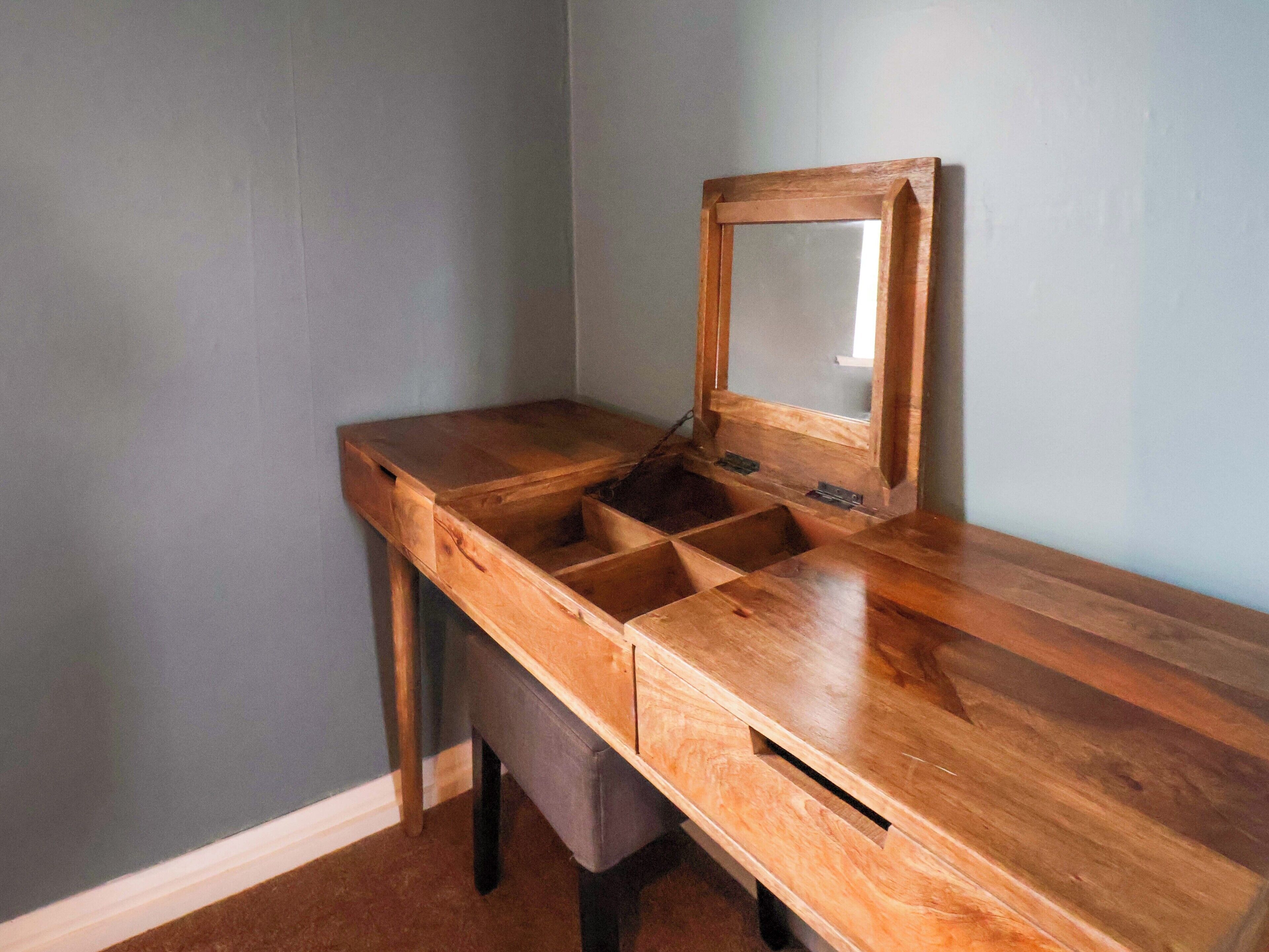 Une coiffeuse en bois avec un miroir et plusieurs compartiments.