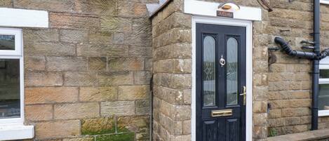 A stone building with a black door, a nameplate above the door, and a small porch area.