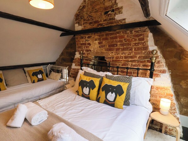 A cozy room with a brick wall, a bed with white bedding, two pillows with a bear design, and a small bedside table with a lamp.