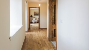 A hallway with wooden flooring, a door on the right, and a window on the left.