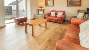 A spacious living room with a wooden floor, a red leather sofa, a plaid armchair, and a wooden coffee table.