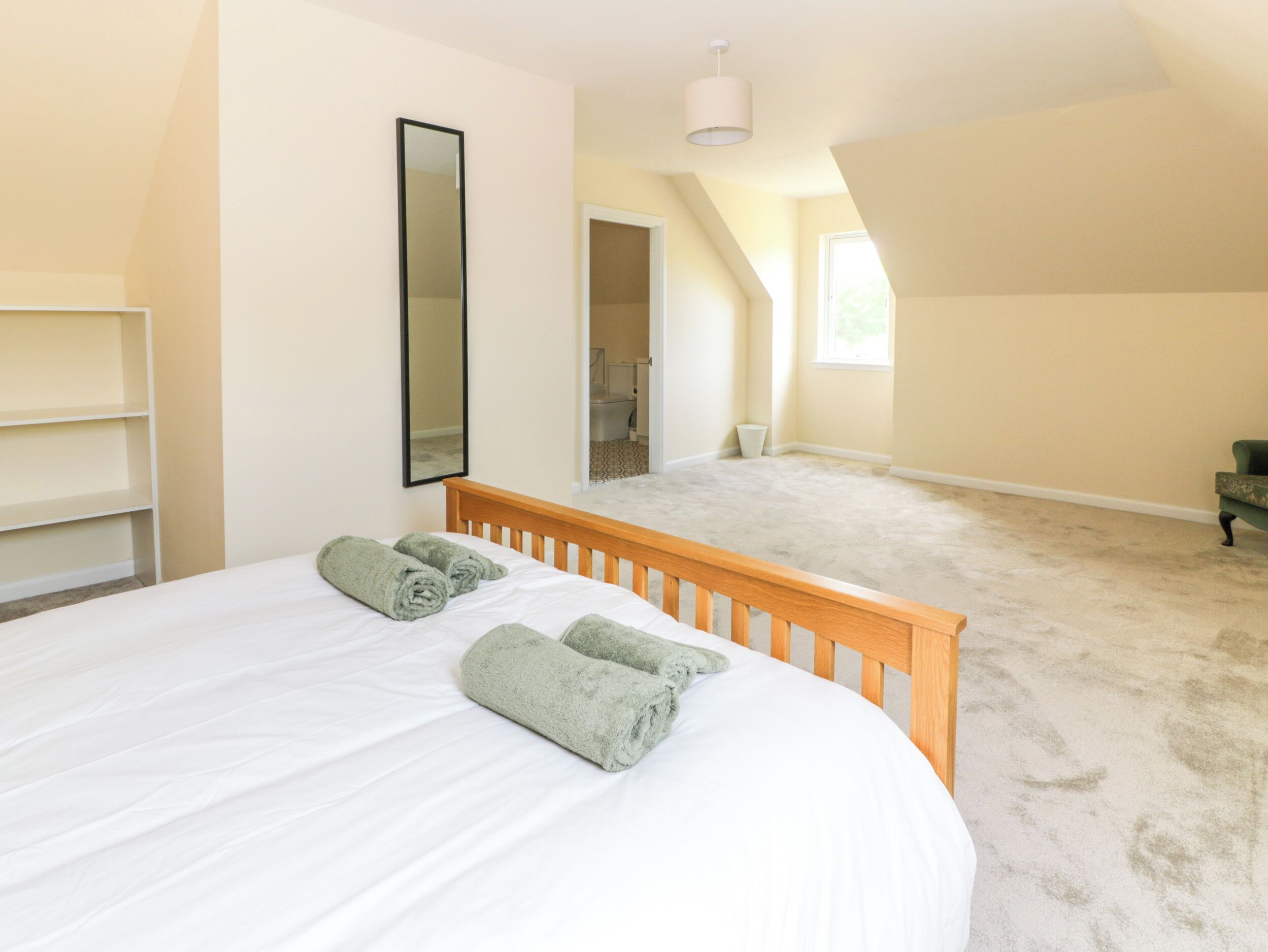 A bedroom with a large bed, a wooden headboard, a mirror, and a view of a bathroom through an open door.
