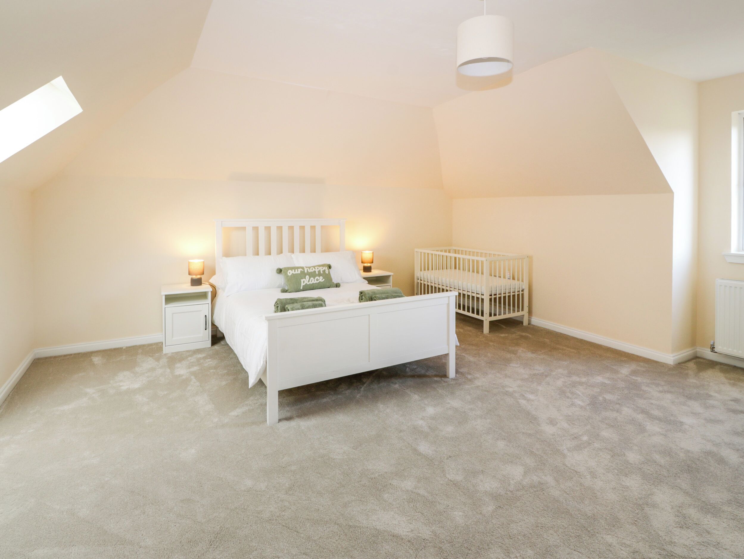 A bedroom with a white bed, a crib, and a skylight.