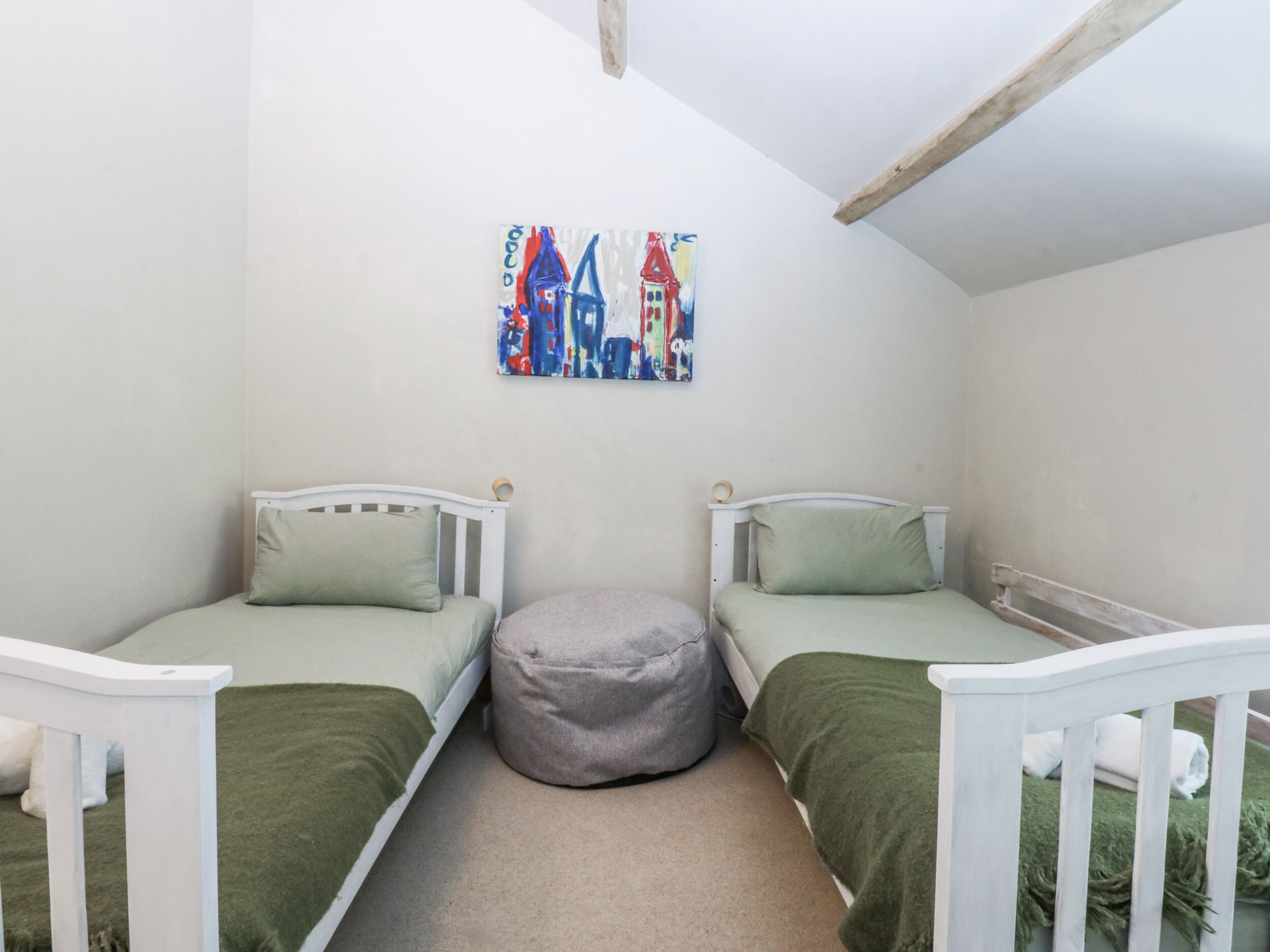 A small, cozy room with two single beds, a green ottoman, and a colorful painting on the wall.