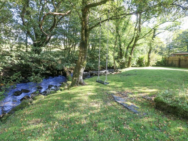 A serene park with a grassy area, a swing, and a stream. - Islwyn (Bala)