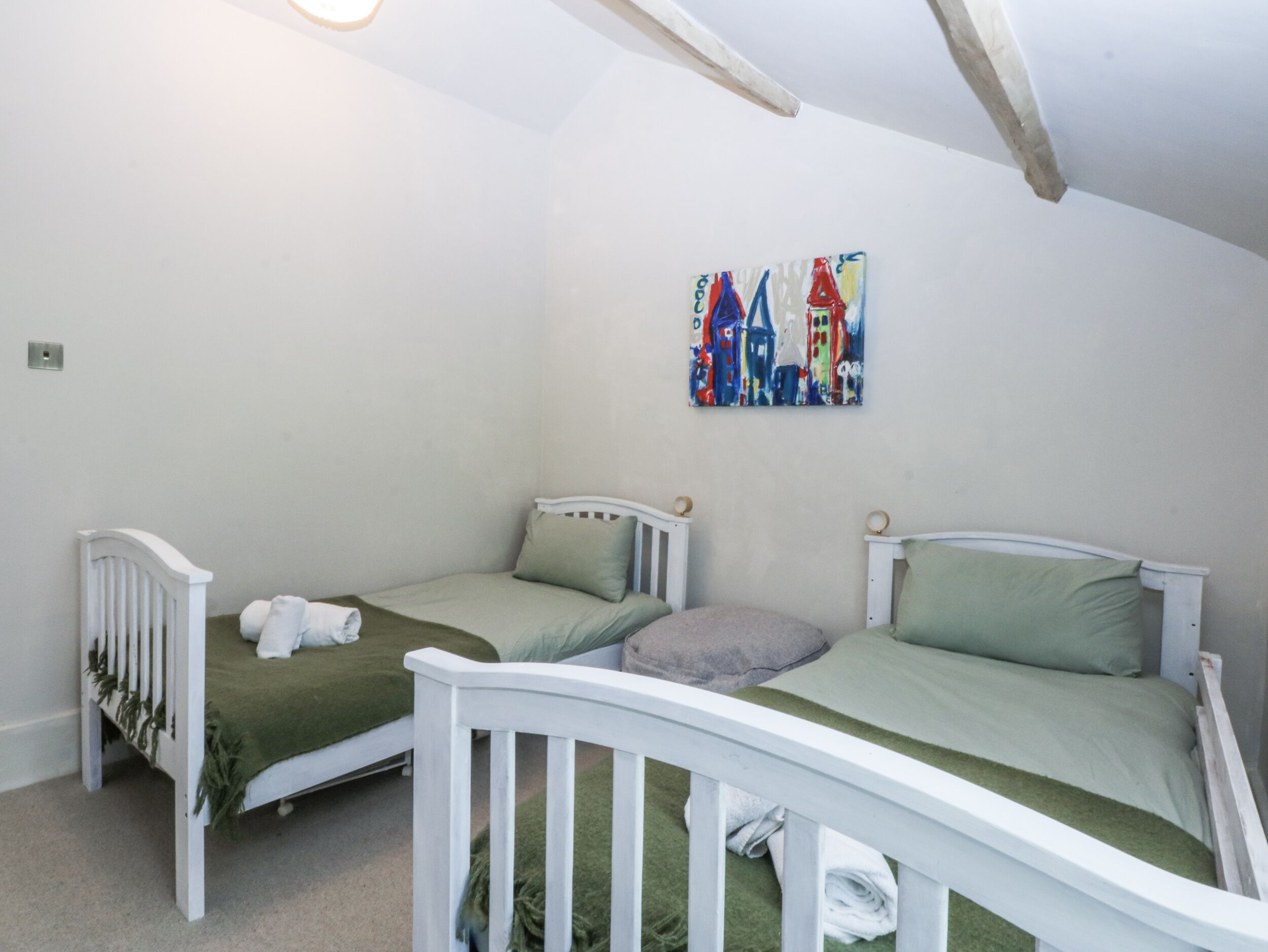 Una habitación con dos camas de madera blanca, cada una con una colcha y almohadas verdes. Encima de las camas hay un cuadro abstracto de colores.