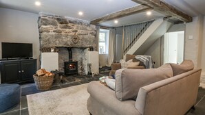A cozy living room with a stone fireplace, a sofa, a television, and a staircase leading upstairs. - Islwyn (Bala)