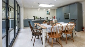 A modern kitchen with a central island, wooden chairs, and pendant lighting. - Islwyn (Bala)