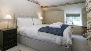 A bedroom with a bed, two bedside tables with lamps, a window, and a stone wall. - Islwyn (Bala)