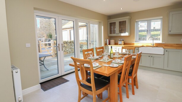A dining area with a table set for six, a kitchen with a sink and cabinets, and a sliding glass door leading to an outdoor patio. - No.8 Cairn Cottage (Leyburn)