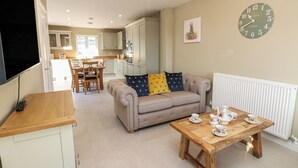 A living room with a sofa, a wooden coffee table with teacups, a clock on the wall, and a kitchen in the background. - No.8 Cairn Cottage (Leyburn)