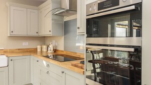 A modern kitchen with light-colored cabinets, a wooden countertop, stainless steel appliances, and a dining area visible through a glass partition. - No.8 Cairn Cottage (Leyburn)