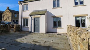 A white building with a stone wall, a wooden gate, and a paved entrance. - No.8 Cairn Cottage (Leyburn)