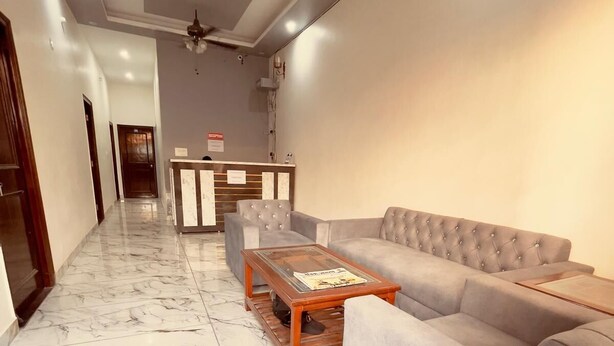 A spacious lobby with a marble floor, a grey sofa, a wooden coffee table, and a reception desk. - Vishram Guest House (Vikasnagar)