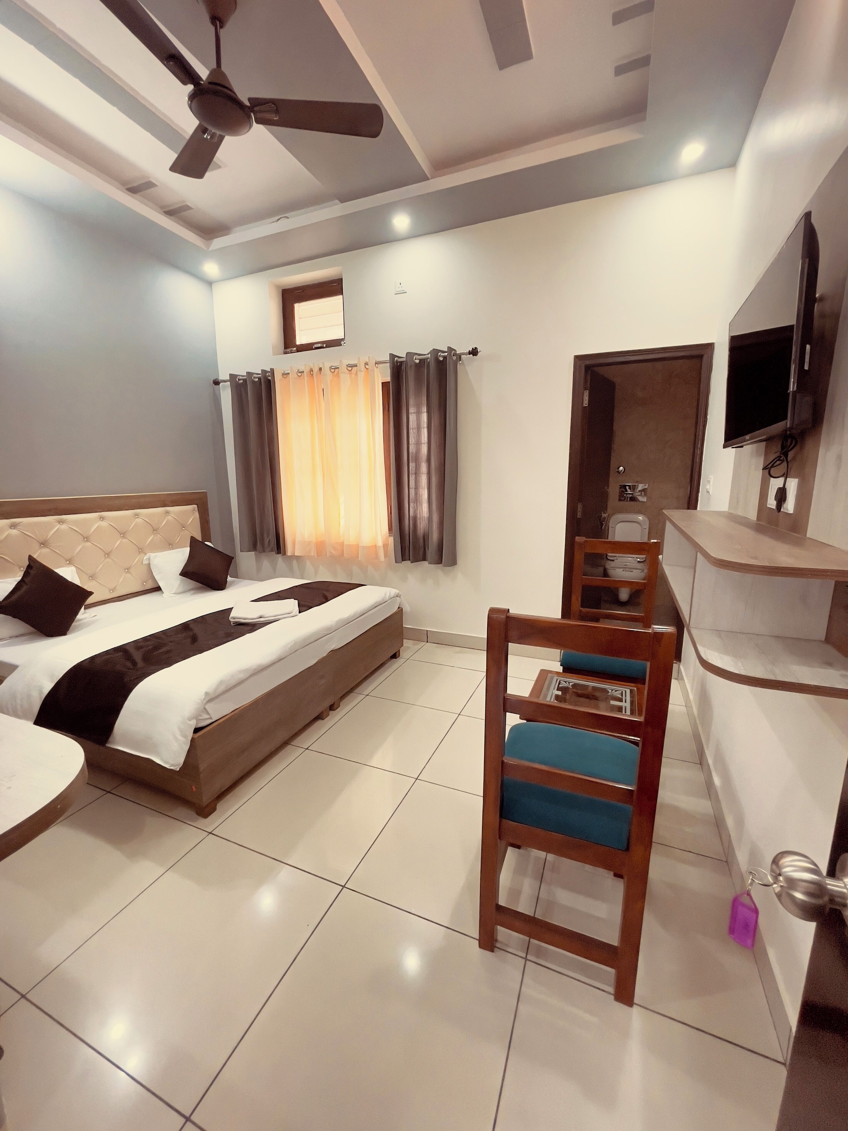 Ein Hotelzimmer mit Bett, Schreibtisch, Stuhl, Deckenventilator, Fernseher und einer Badezimmertür.