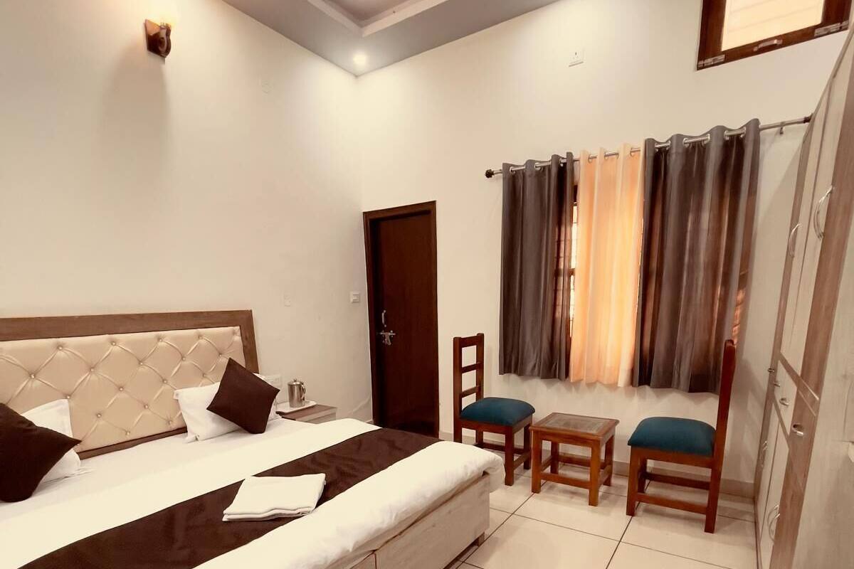 A bedroom with a large bed, a small table, two chairs, a window with curtains, and a door.