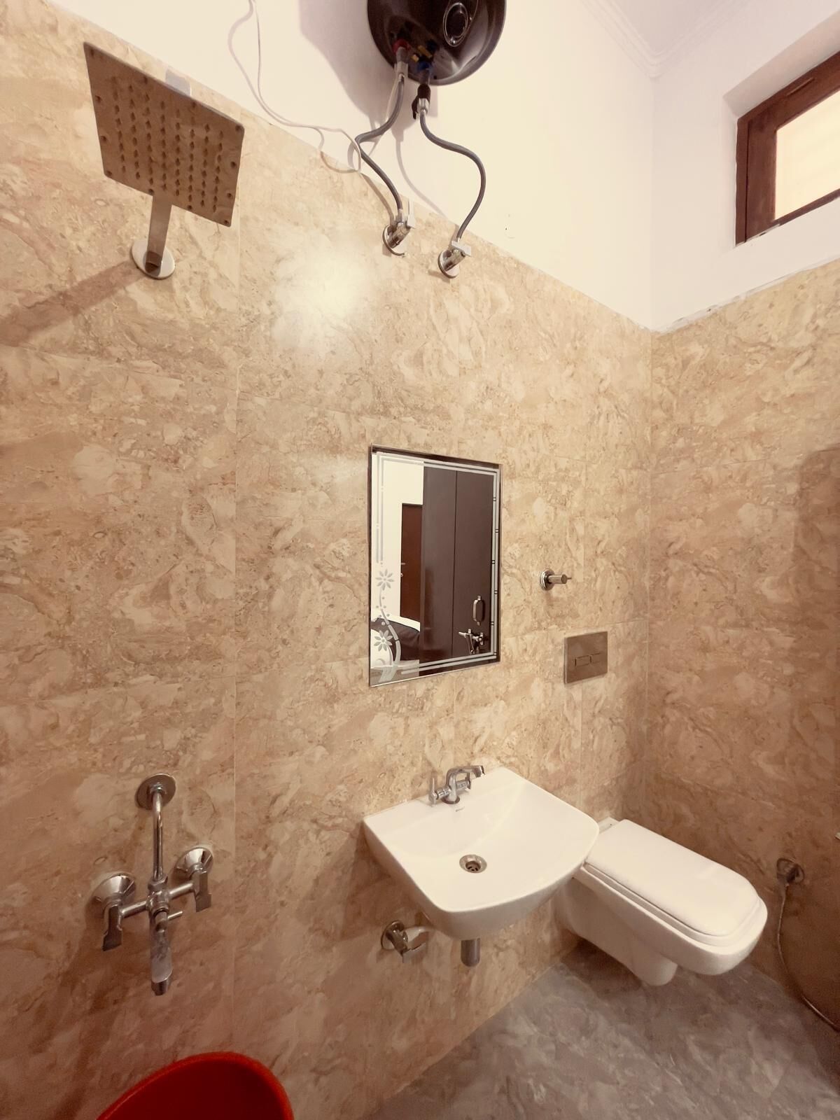 A bathroom with a marble wall, a sink, a toilet, a mirror, and a shower head.