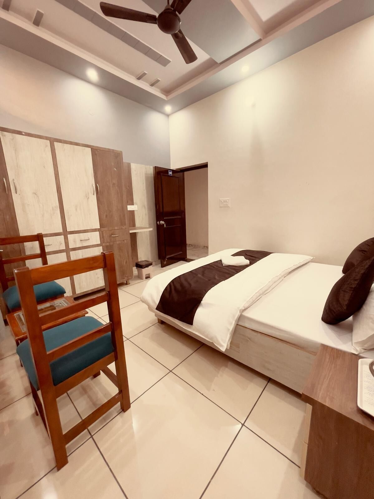 A modern bedroom with a bed, a wooden chair, a wardrobe, and a ceiling fan.