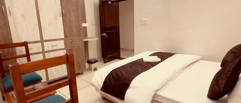 A modern bedroom with a bed, a wooden chair, a wardrobe, and a ceiling fan.