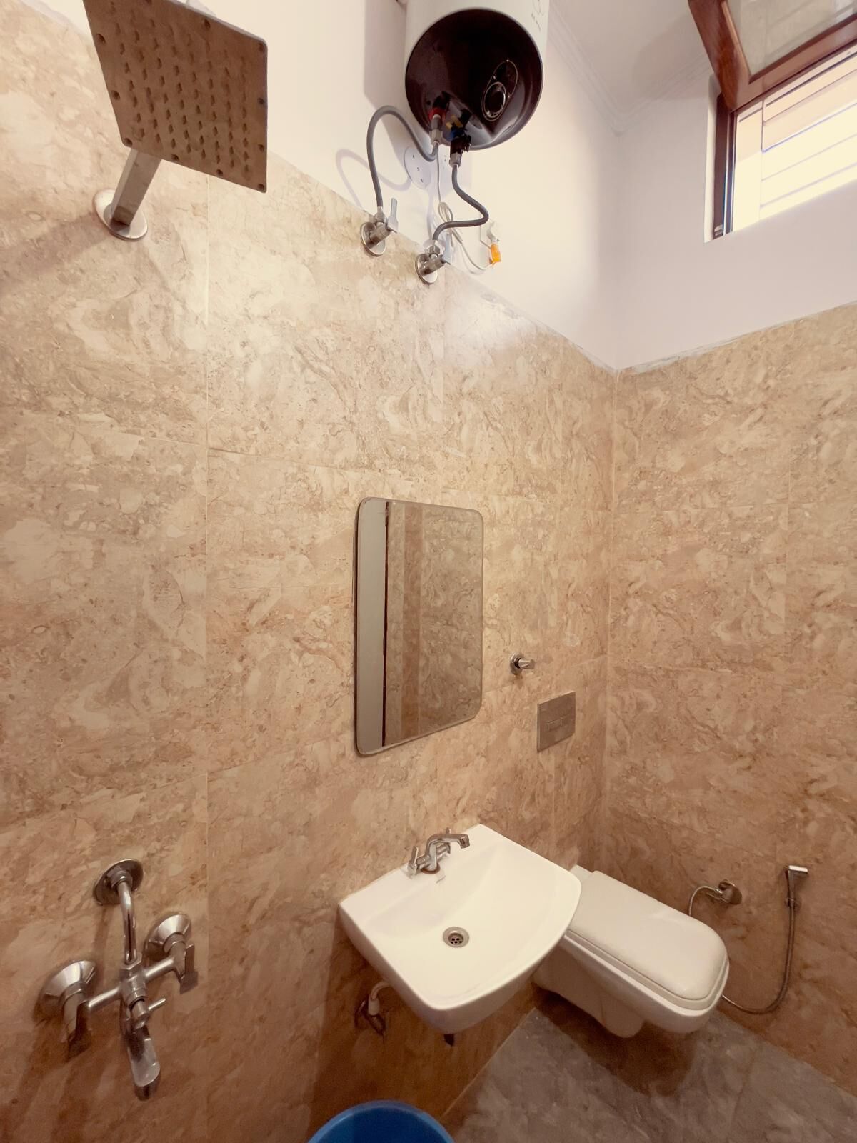 Un baño con pared de mármol, lavamanos, inodoro, ducha y espejo.