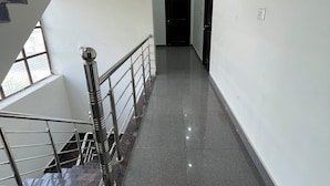 A modern hallway with a staircase on the left, a door at the end, and a light fixture on the ceiling. - Vishram Guest House (Vikasnagar)