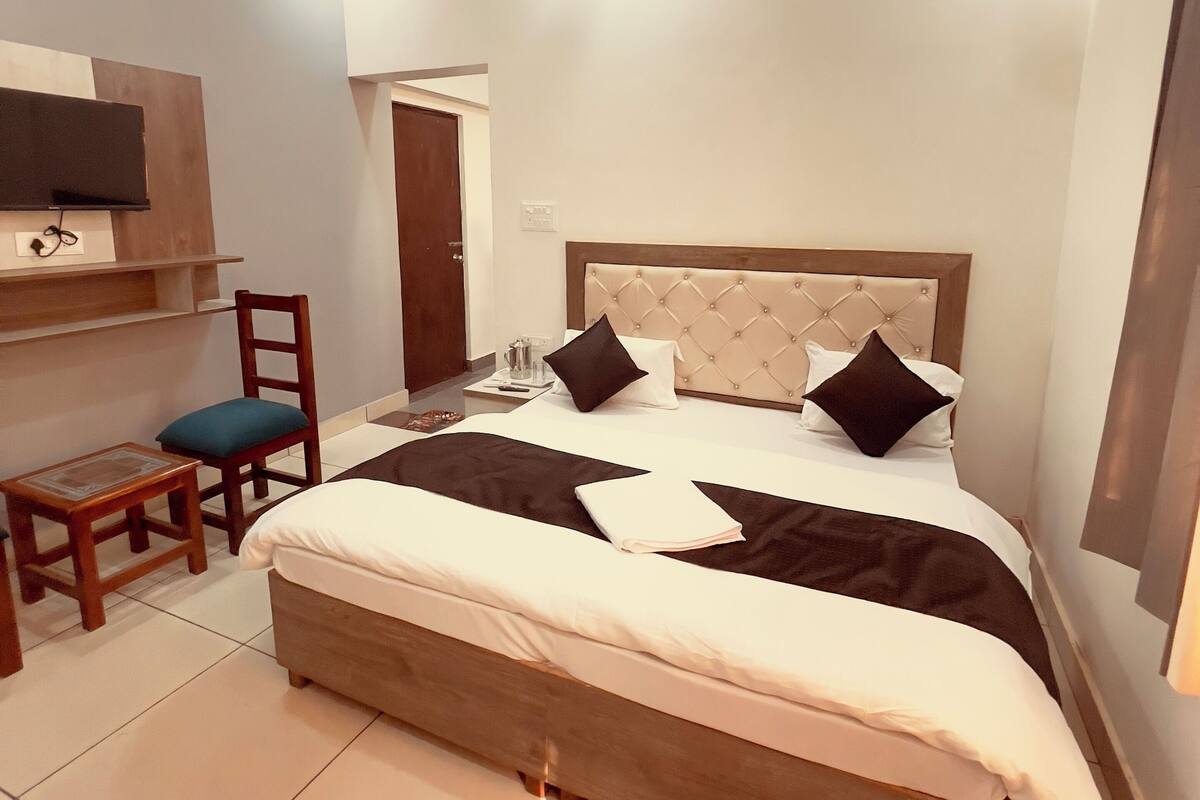 A neatly arranged bedroom with a bed, a chair, a small table, a ceiling fan, and a mounted TV.