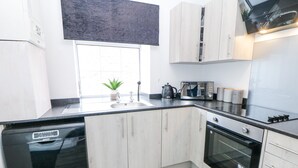 Een moderne keuken met witte kasten, een vaatwasser, een oven en een raam met een plant op het aanrecht.