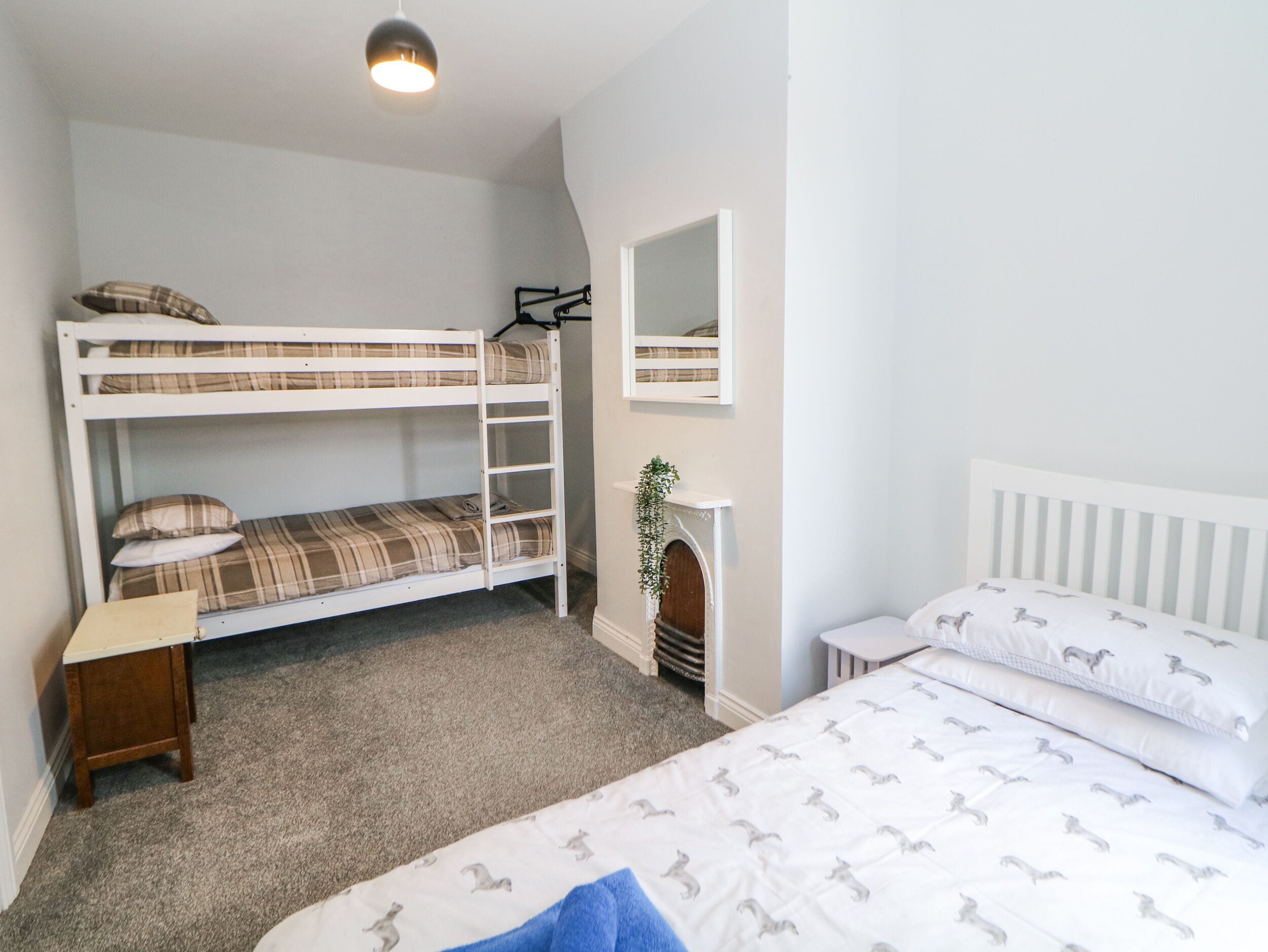 Een slaapkamer met een stapelbed, een eenpersoonsbed, een klein tafeltje en een spiegel aan de muur.