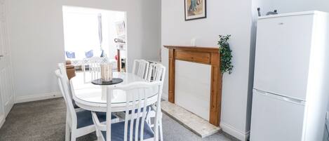 A dining area with a white table and chairs, a wooden fireplace, and a white refrigerator.